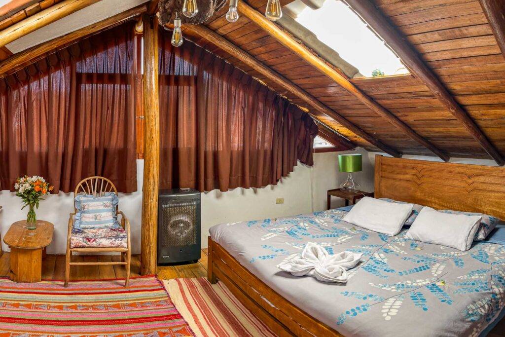 Accommodation in Cusco Andean top expeditions– rustic attic room with wooden ceiling, cozy double bed, and warm decor.